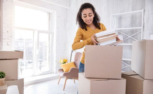 Cute curly-haired girl packing books before moving out 